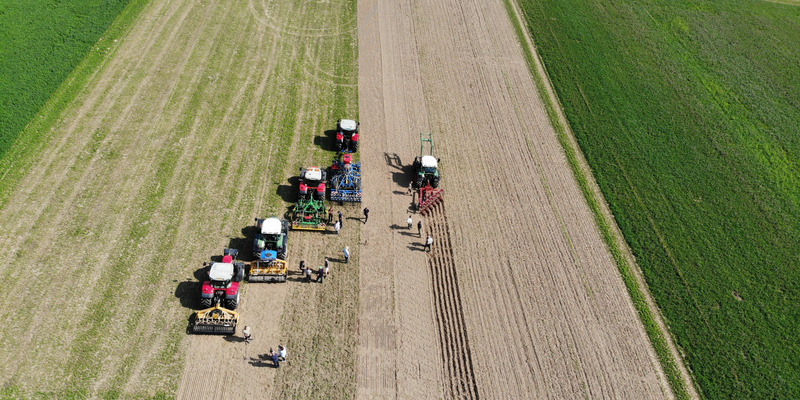 Luftaufnahme von mehreren Traktoren und Personen auf einem Feld.